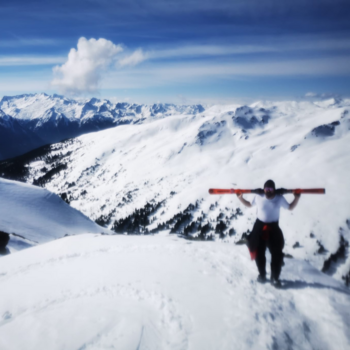 Mann steht mit Skiern über den Schultern an verschneitem Berghang