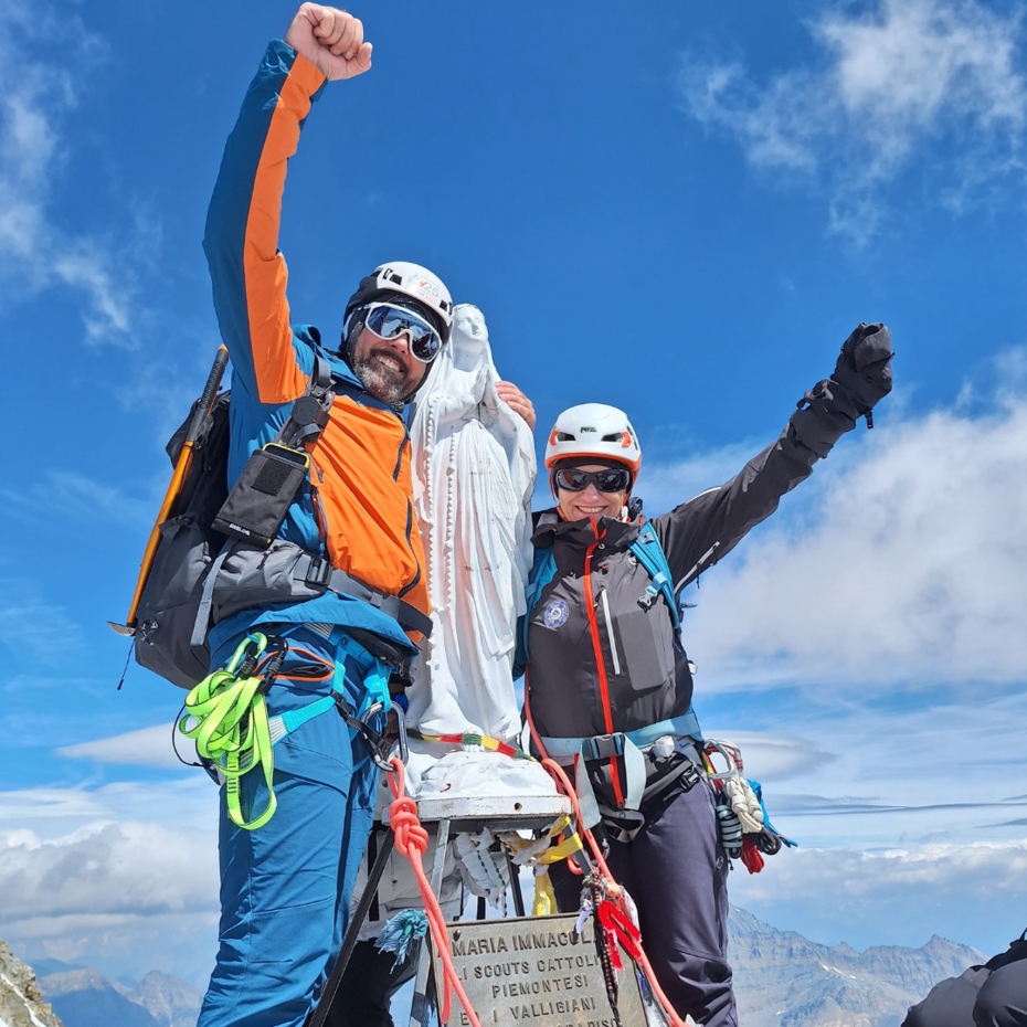 Ein lächelnder Mann und eine lächelnde Frau strecken eine Faust in den Himmel neben der Madonna auf dem Gipfel des Gran Paradiso