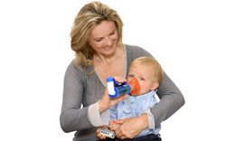 Mother holding asthma spray with spacer and mask in front of baby’s face on her arm