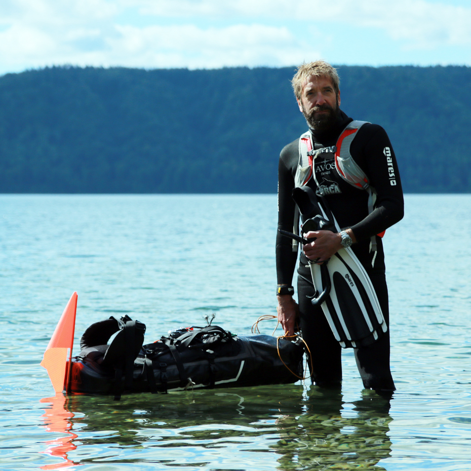 Ein Taucher steht im Wasser, neben ihm schwimmt ein wasserdichter Rucksack
