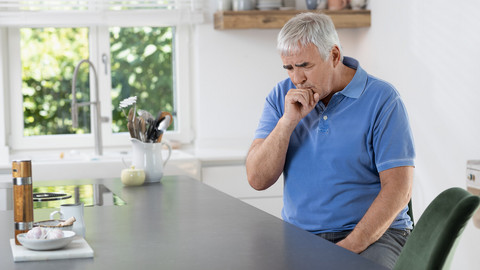 Elderly man sitting in the kitchen while coughing