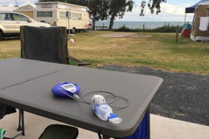 Inhalationsgerät liegt auf Campingtisch, im Hintergrund sind Camper und ein See