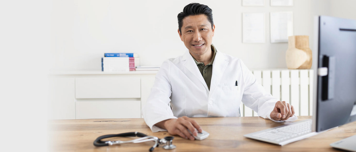 Ein Arzt sitzt in seiner Praxis am Schreibtisch und arbeitet am Computer