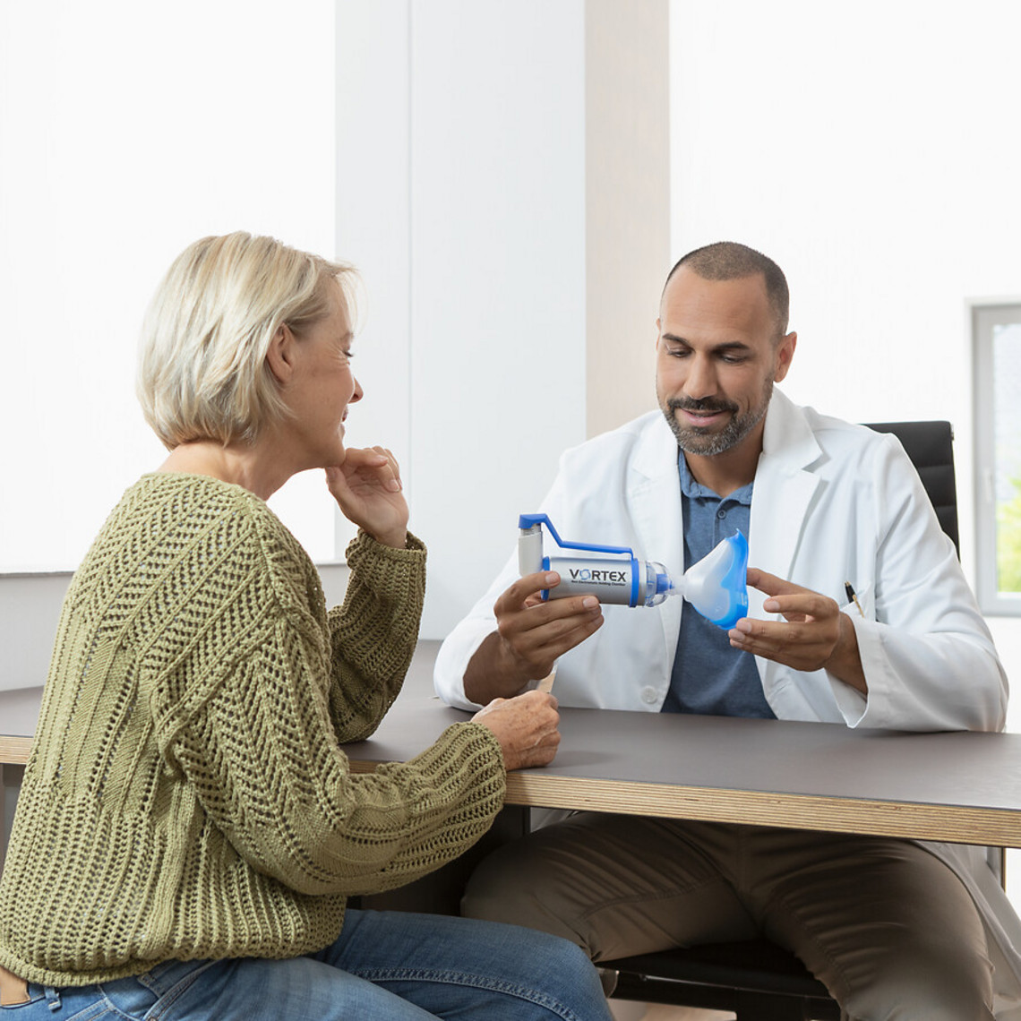 Urlaub mit COPD: Notfallplan mit Arzt besprechen Ältere Frau sitzt vor ihrem Arzt, der ihr die VORTEX Inhalierhilfe erklärt