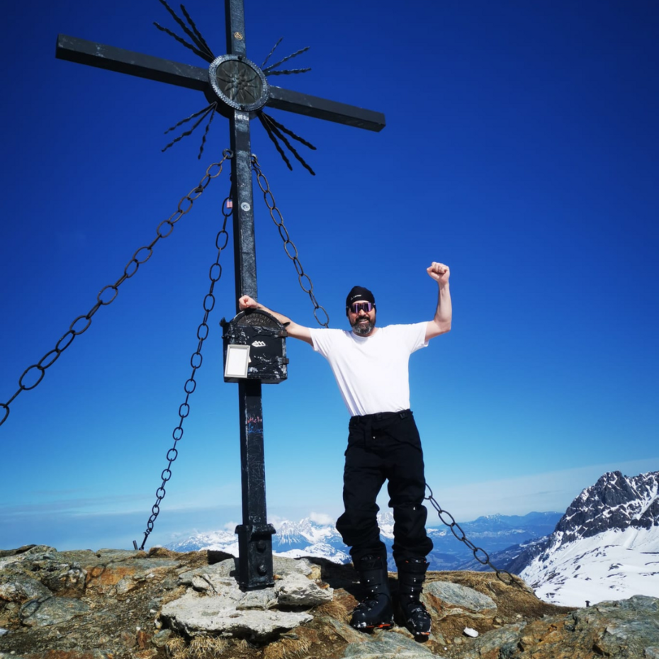 Bernhard Kaut auf dem Endspurt: Salzburger Pinzgau Mann steht neben Gipfelkreuz und streckt die Faust in die Luft