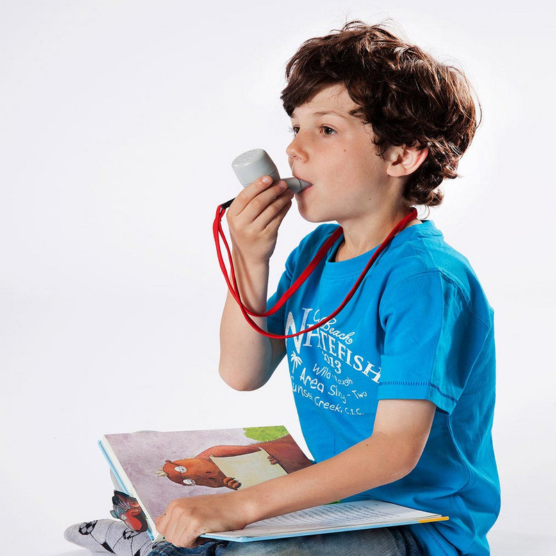 Ein Junge sitzt im Schneidersitz. Er sitzt aufrecht, der Kopf zeigt gerade und benutzt das PARI O-PEP dessen Mundstück er mit seinen Lippen umschließt.