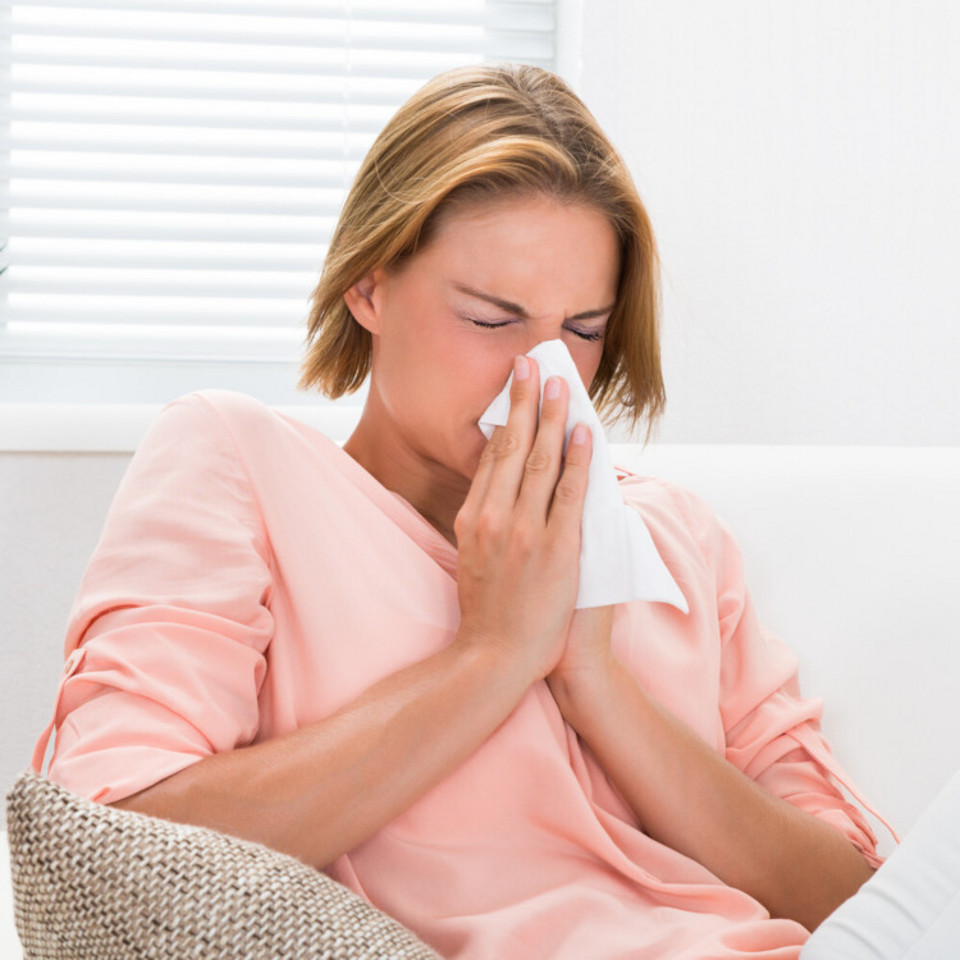 What you should do if you have a blocked nose because of an allergy: Helpful tips Frau sitzt auf Sofa und schnupft in ein Taschentuch, das sie mit beiden Händen vor ihre Nase hält