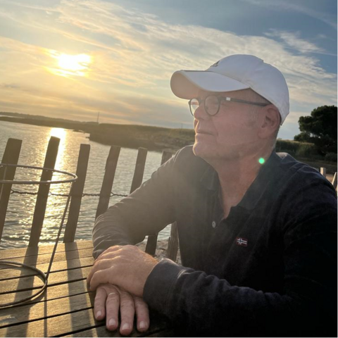 Mann sitzt an einem Tisch am Seeufer und schaut hinaus auf den See