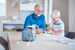 Grandpa playing with grandson at the table in the background, an inhaler with nebuliser in the foreground.