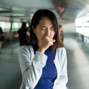 Junge Frau hält sich an öffentlichem Ort beim Husten die Hand vor den Mund