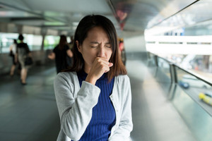 Young woman holds her fist in front of her mouth while coughing in public place