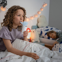 Kind sitzt im Bett und nutzt ein PARI BOY Go Inhalationsgerät mit Mundstück, weiteres Kind liegt im Hintergrund.