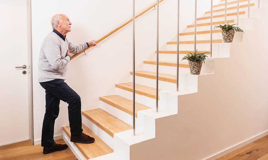Ein alter Mann mit Atemwegsbeschwerden steht vor einer Treppe und sieht nach oben
