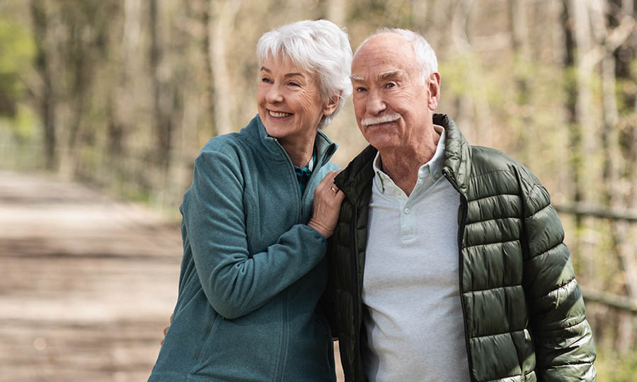Ein älteres Ehepaar steht einander zugewandt im Wald und erfreut sich an der Natur