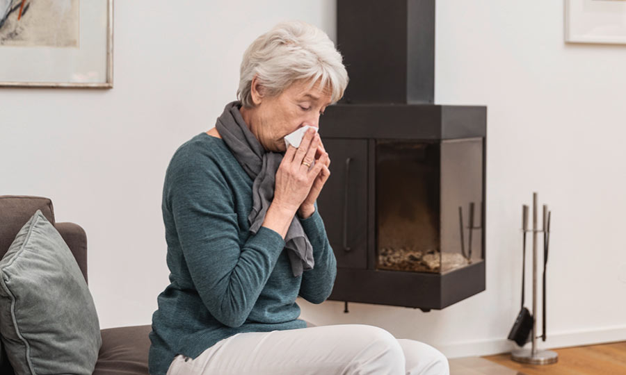 Eine Frau mit Erkältung sitzt auf dem Sofa und reinigt sich mit einem Taschentuch die Nase