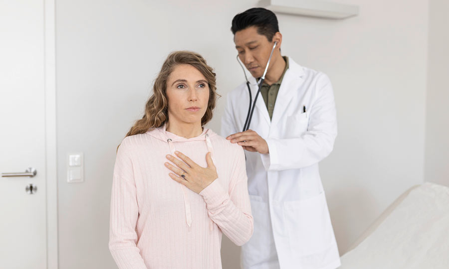 Arzt untersucht Patientin mit Mukoviszidose. Patientin hat dabei die Hand an ihrer Brust.