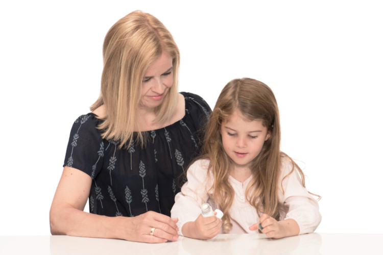 Mutter schaut Tochter zu, die Asthmaspray in der Hand hält und untersucht