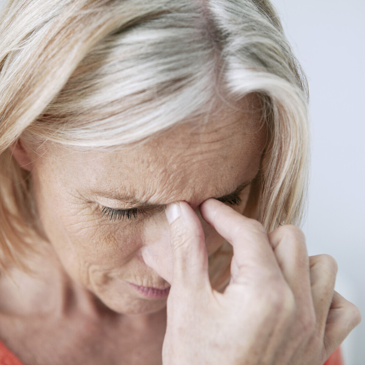 Ältere Frau in Nahaufnahme hält sich die Nasenwurzel und scheint Schmerzen zu haben