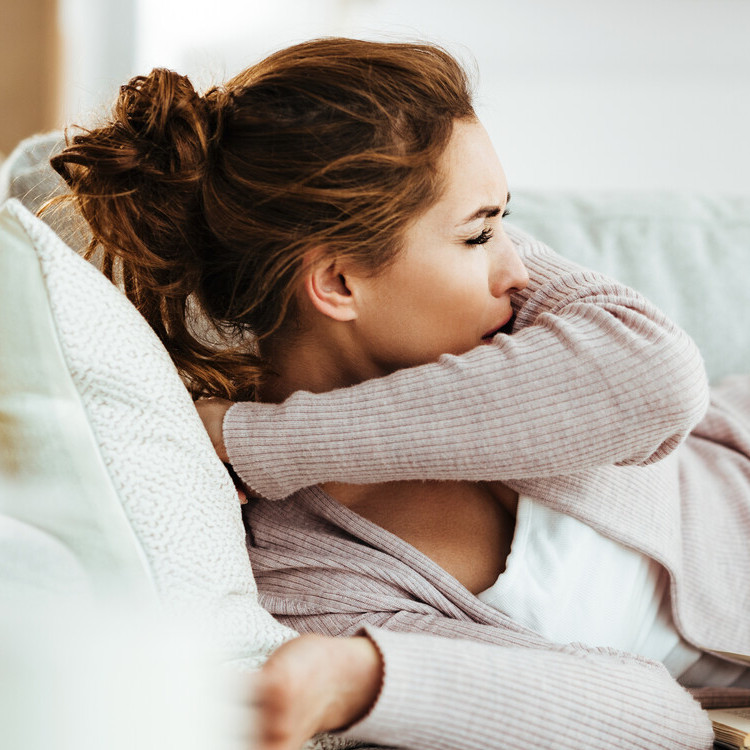 Frau liegt im Bett und hustet in die Armbeuge