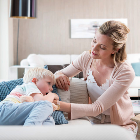 Ein kranker Junge liegt mit Teddy auf dem Sofa und wird von seiner Mutter getröstet