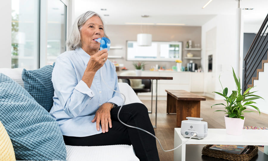 Ältere Frau sitzt auf Sofa und inhaliert isotone Salzlösung zur Unterstützung der Abwehr
