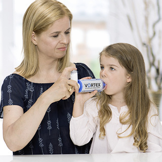 Eine Mutter hilft ihrer jungen Tochter bei der Inhalation mit einer VORTEX Inhalationshilfe. Die Mutter hält das Dosieraerosol, während das Kind durch das Mundstück atmet.