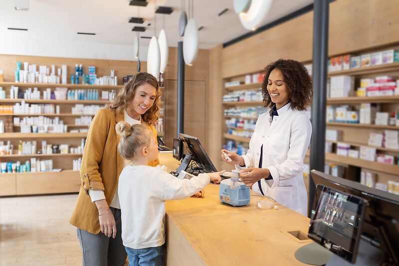 Eine Apothkerin erklärt den PARI COMPACT2 einer jungen Mutter und ihrem Kind