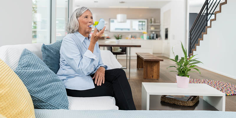 Eine ältere Dame sitzt auf einem Sofa und inhaliert mit dem PARI BOY free