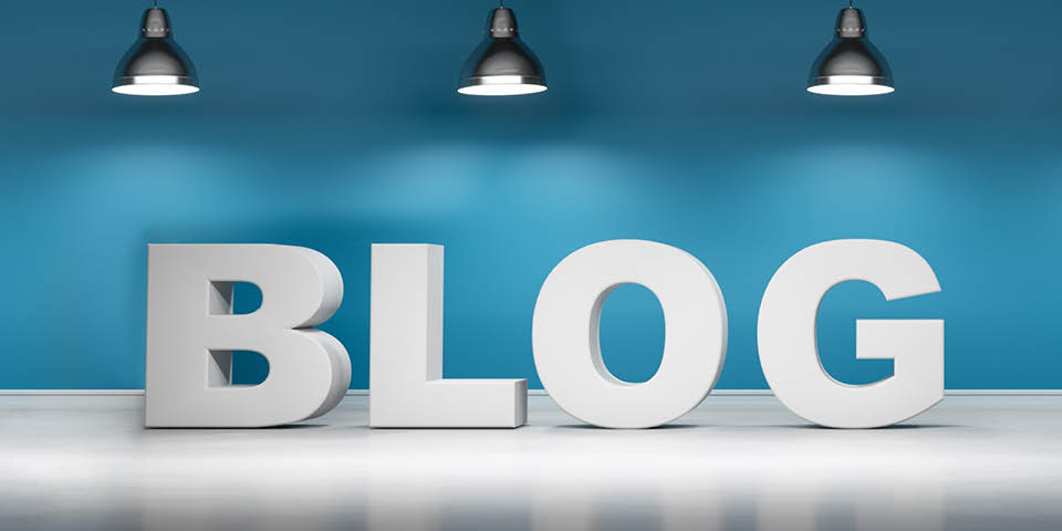 Große weiße Buchstaben bilden das Wort BLOG vor einer blauen Wand, beleuchtet von drei Deckenlampen.