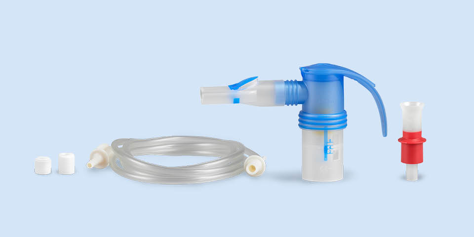 Produktabbildung: Vor einem blau-grauen Hintergrund steht rechts ein PARI LC SPRINT Vernebler mit Mundstück. Links liegt der dazugehörige Anschlussschlauch. Daneben stehen noch zwei Austauschfilter für den Kompressor. Zusammen bilden sie ein PARI Vernebler Year Pack.