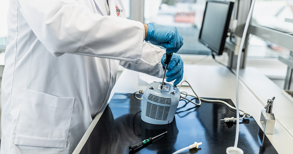 Person im Service mit Laborkittel und Handschuhen repariert einen PARI COMPACT2 auf einem Arbeitstisch mit Werkzeugen.