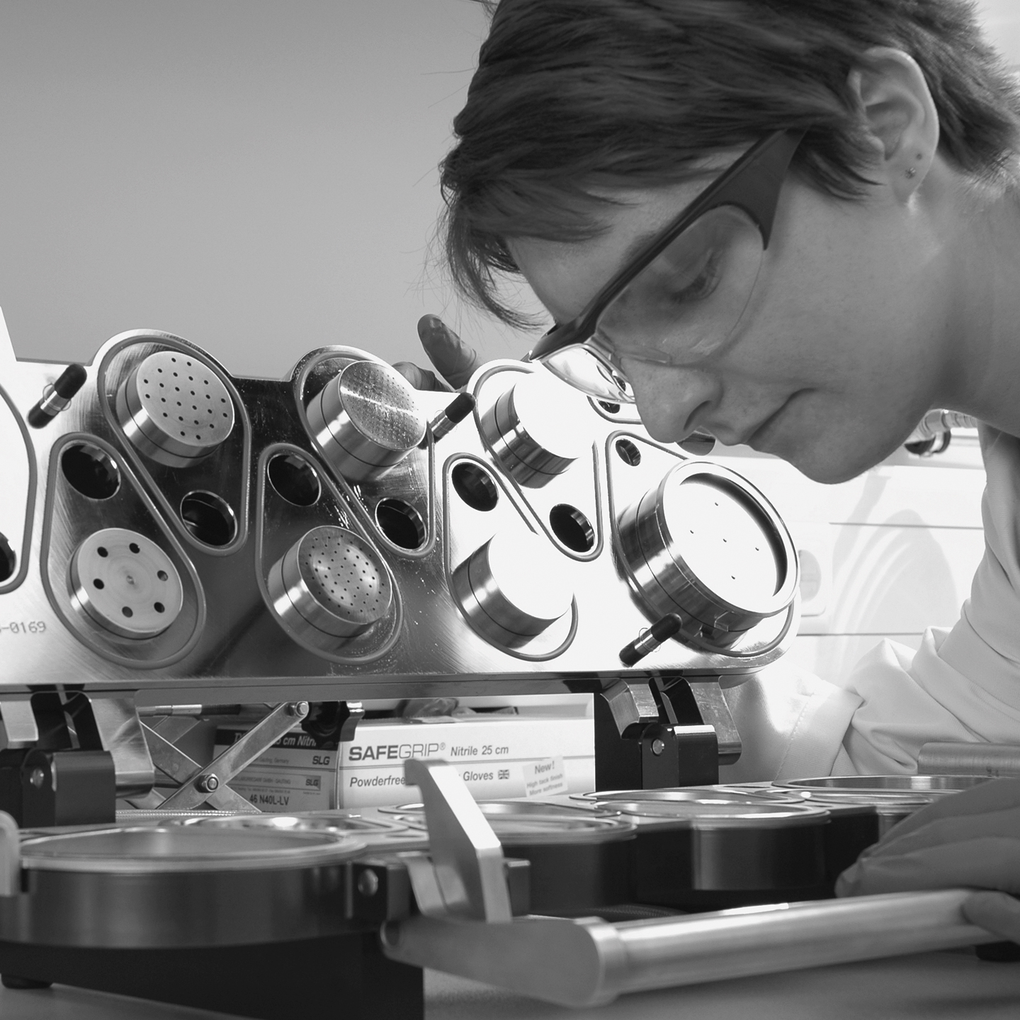 Person arbeitet an einem Laborgerät mit mehreren runden Metallkammern und Lochplatten auf einer Halterung.