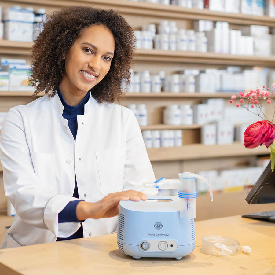 A pharmacist demonstrates a PARI COMPACT2 inhalation device on a counter in the pharmacy.
