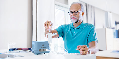 A older man is prepairing a compact2 nebuliser with saline