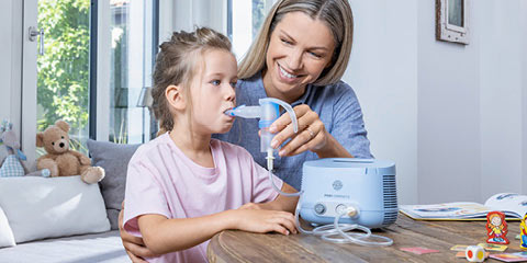 A young mother helps her daughter inhale with a PARI Compact2 inhalation device