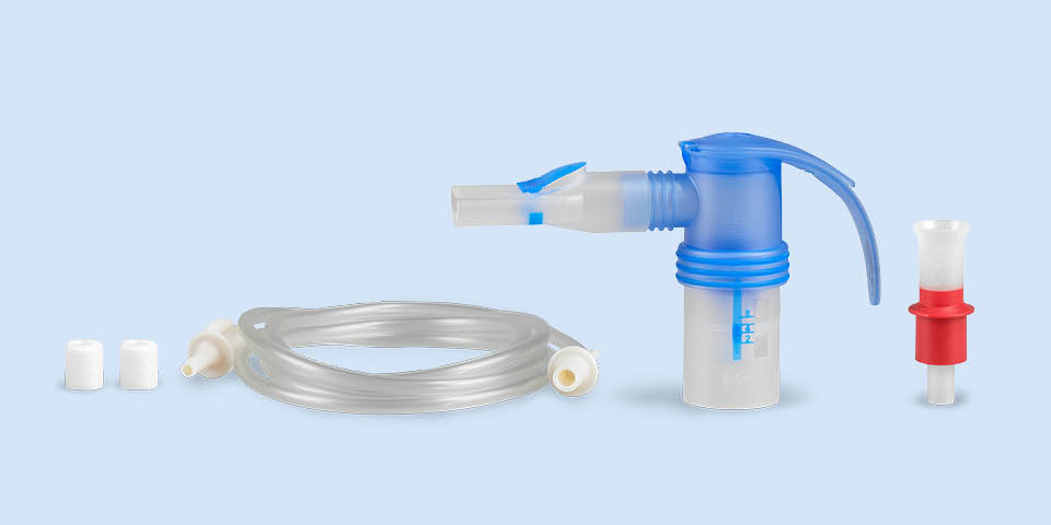 Imagem do produto: Num fundo azul-acinzentado, encontra-se no centro um nebulizador PARI LC SPRINT com bocal. À direita, um bocal vermelho. À esquerda, encontra-se a mangueira de ligação, ao lado de dois filtros diferentes para o compressor.