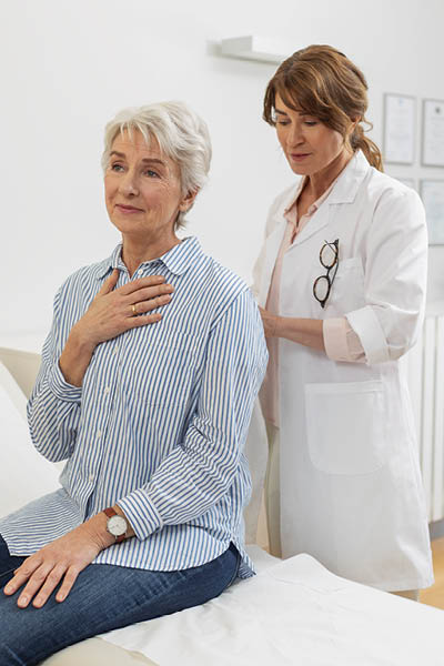 A doctor examines a seated person and places a stethoscope against their back for a medical examination.